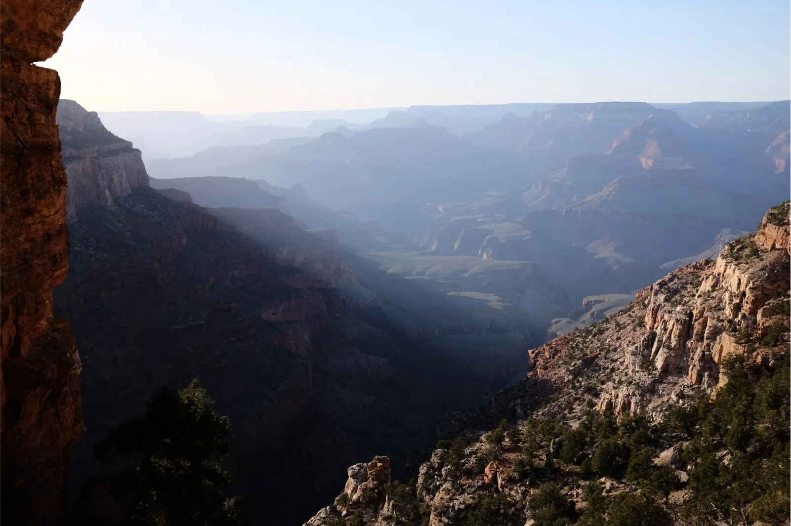 A photo taken from along the ridgeline of the Grand Canyon looking out across the valley through a light haze.